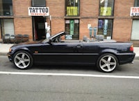 a black bmw convertible parked in front of a tattoo shop